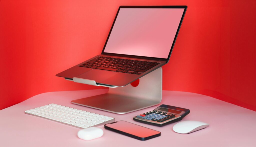 Sleek modern workspace with a laptop, keyboard, mouse, and calculator in a vibrant red setting.