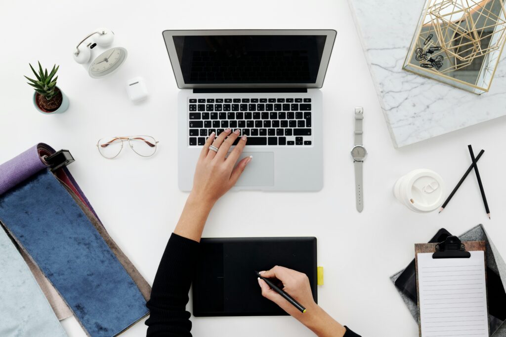 Overhead view of a creative workspace with laptop, drawing tablet, and office accessories on a white desk.
